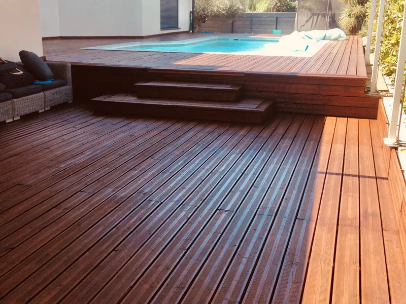 Terrasse en lames de bois teinté au soleil, avec quelques marches menant à une piscine