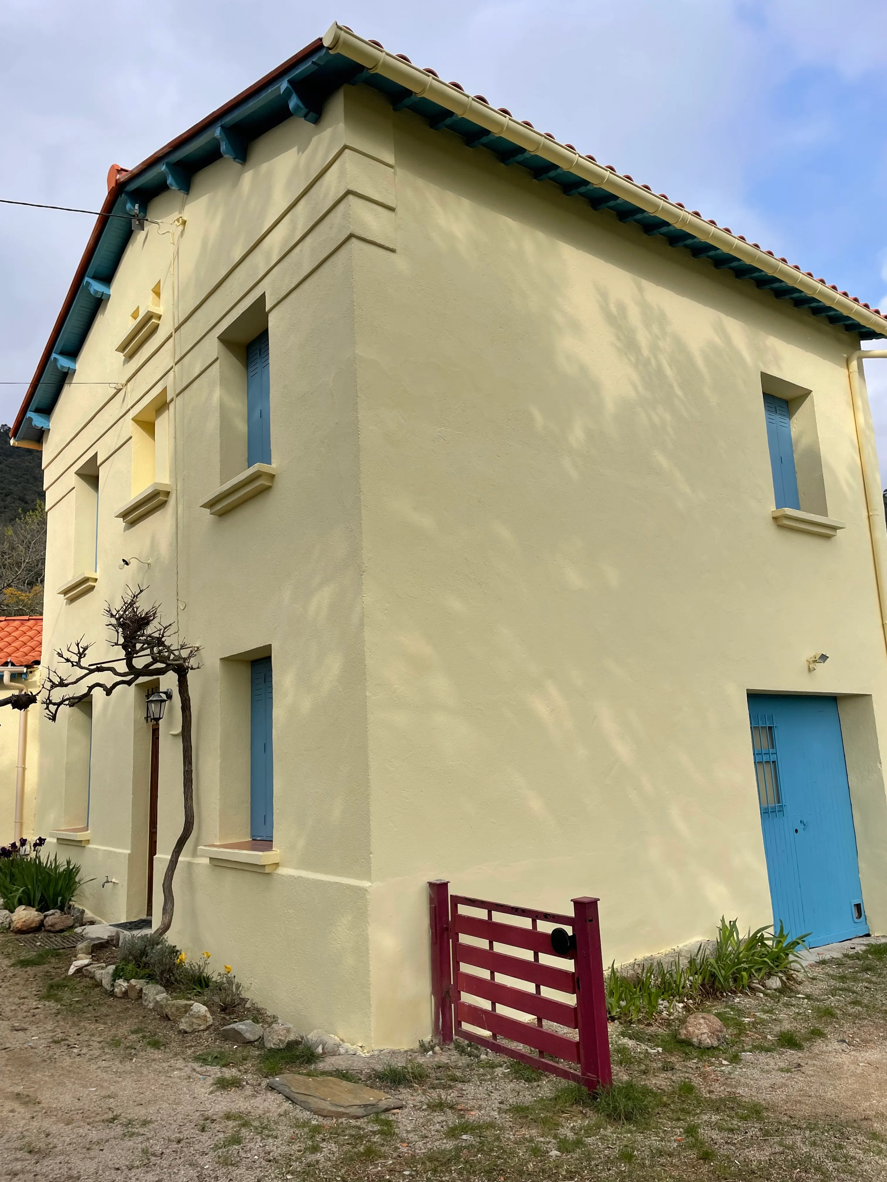 Façade de maison en enduit jaune pâle aux volets bleus, après ravalement