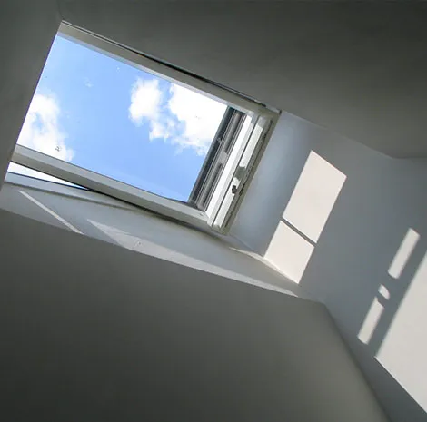 Fenêtre de toit ouverte sur le ciel, vue depuis l’intérieur d’une pièce aux murs blancs
