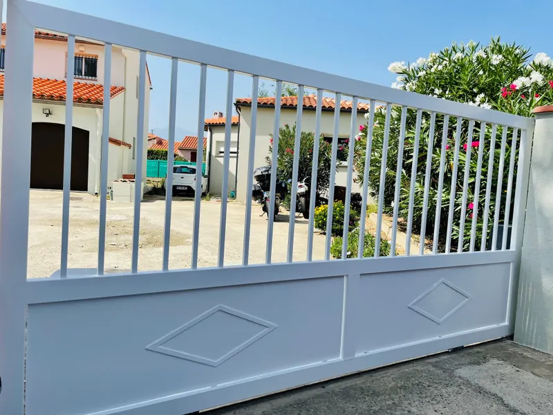 Portail en métal blanc à barreaux, soubassement plein orné de deux losanges
